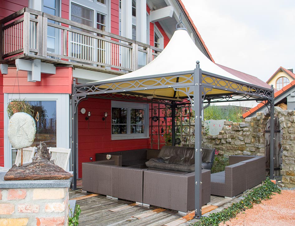 Ein wetterfester Pavillon mit festem vanillefarbenem Dach auf einer Holzterrasse.